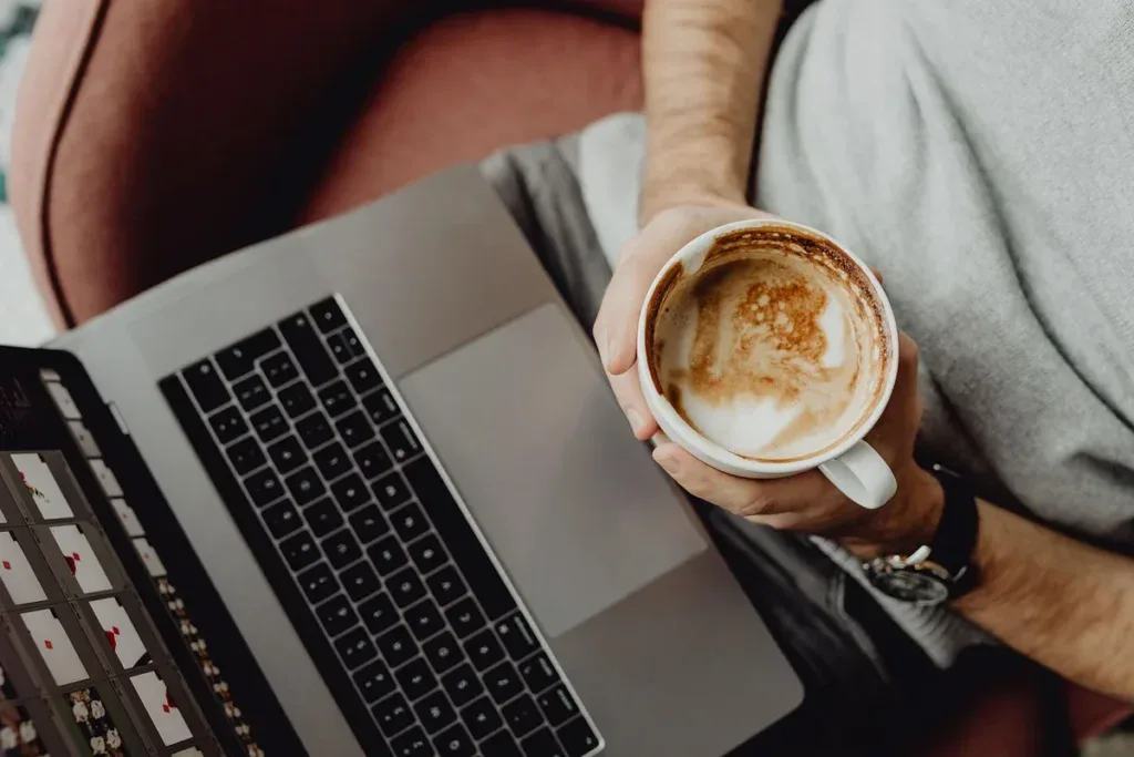 Kawa w dłoni i laptop na kolanach, kofeina i długi czas przed ekranem