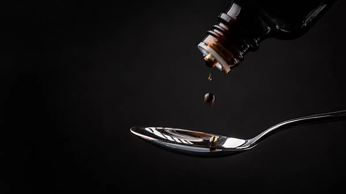 Syrop na mokry kaszel kapiący z butelki na łyżkę